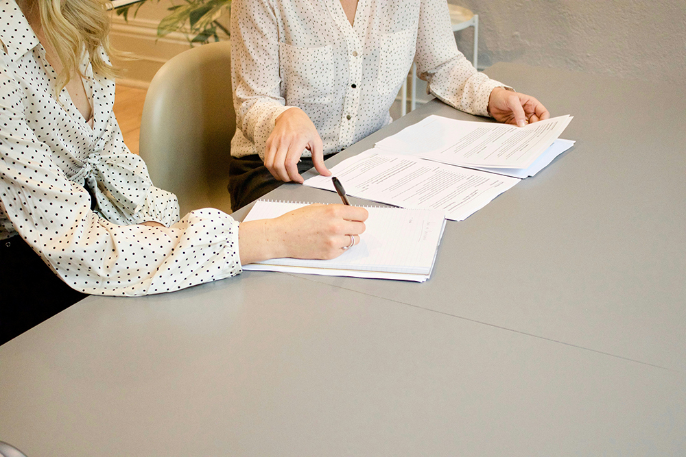 Two professionals sitting at a table discussing documents, emphasizing the importance of clear communication and collaboration.