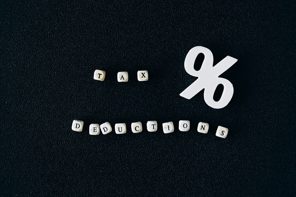 White letter blocks spelling 'TAX DEDUCTIONS' on a black background with a large white percentage symbol, representing financial savings and tax benefits.