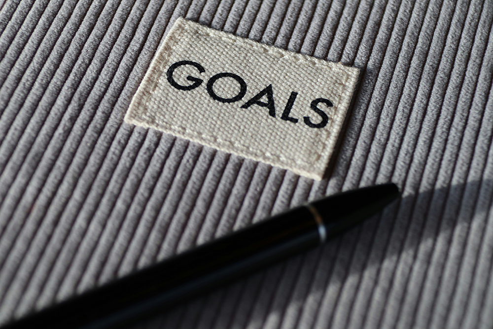 A fabric patch with the word "GOALS" printed on it, placed on a textured surface with a pen nearby, symbolizing strategic planning and goal setting.