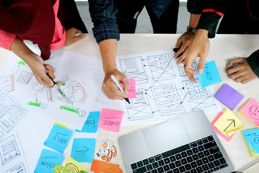 Team collaborating on UX design with flowcharts, sticky notes, and wireframes to plan user experience journeys.