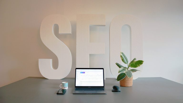 The letters SEO on a desk beside a laptop